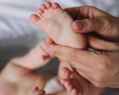 Photo d'un pied d'enfant tenue par une main adulte pendant une prestation de réflexologie plantaire